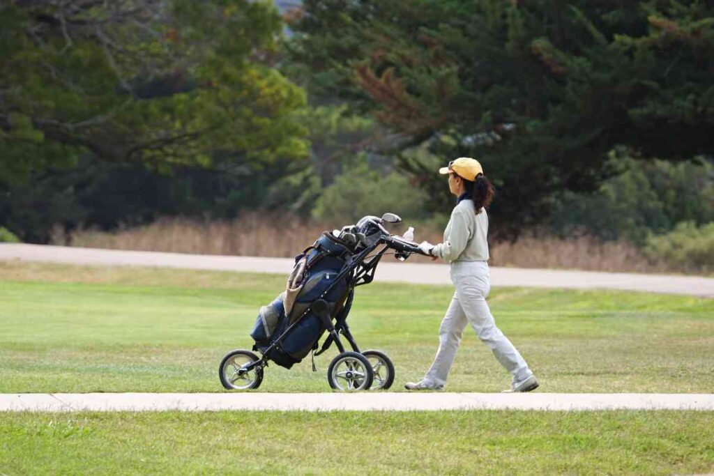 golfer pushing a pushcart with golf clubs
